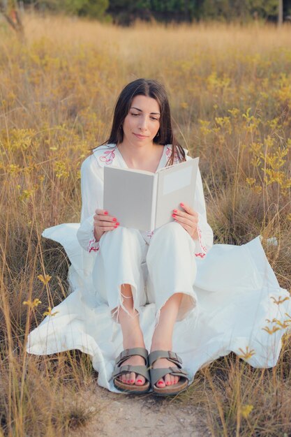 Femme avec un livre lisant sur un pré au coucher du soleil