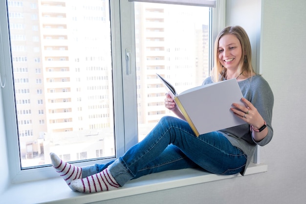 Femme avec un livre photo dans ses mains sur le rebord de la fenêtre à l'intérieur