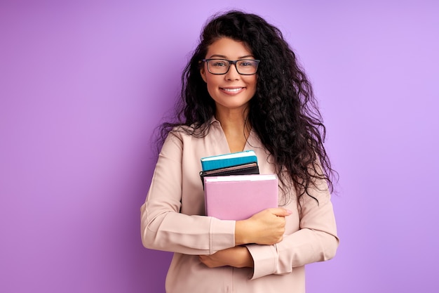 Femme avec des livres isolés sur un mur violet, aime l'éducation, étudie. étudiante en chemisier