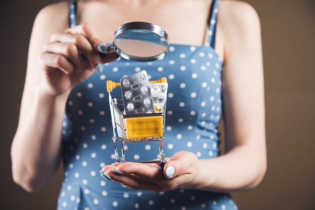 Une femme avec une loupe regarde un chariot de comprimés. concept de recherche d'achat de drogue