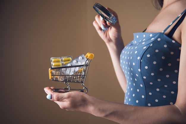 Une femme avec une loupe regarde un chariot de comprimés. concept de recherche d'achat de drogue