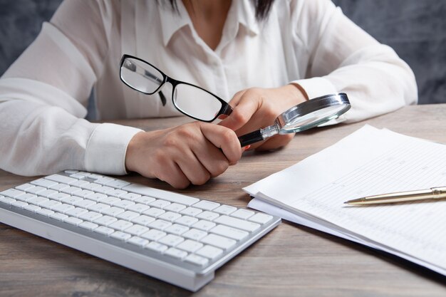 Femme avec une loupe regarde le papier sur le bureau