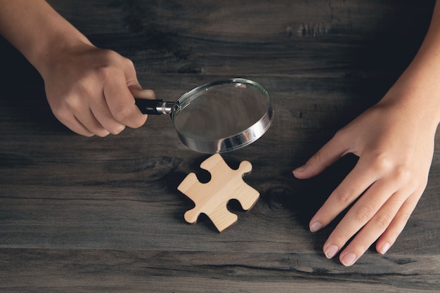 Une femme avec une loupe regarde une pièce de puzzle