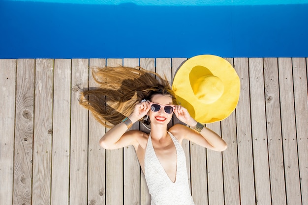 Femme ludique allongée avec un chapeau jaune au bord de la piscine. Concept de vacances d'été