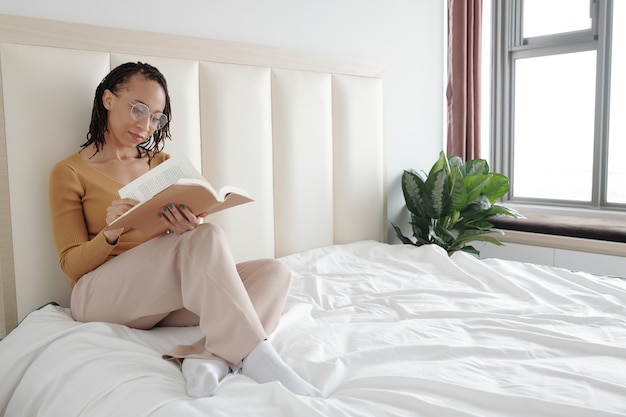 Femme à lunettes assise sur le lit et livre de lecture pour sa recherche