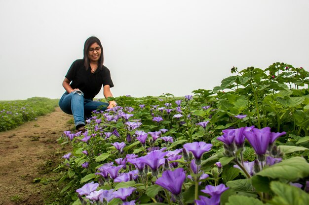 Femme avec des lunettes assise touchant des fleurs lilas sur un sentier ciel nuageux