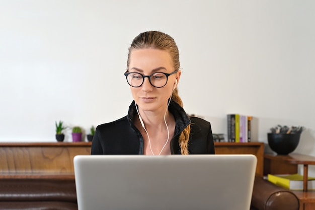 Femme avec des lunettes et des écouteurs et un ordinateur portable étudie le travail en ligne