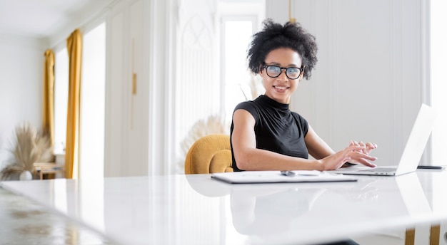 Une femme avec des lunettes est une secrétaire en ligne travaillant dans un nouvel espace de coworking de bureau à l'aide d'un ordinateur portable