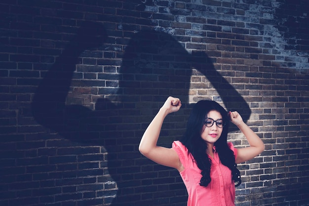 Une femme à lunettes lève les mains et montre des muscles fiers de ses réalisations