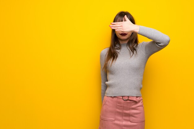 Femme avec des lunettes sur un mur jaune couvrant les yeux à la main. Je ne veux pas voir quelque chose