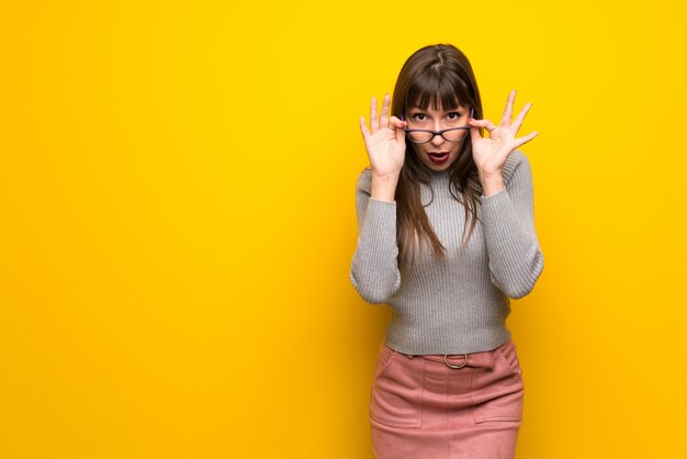 Femme avec des lunettes sur un mur jaune avec des lunettes et surpris