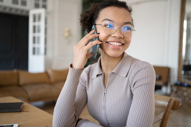Une femme avec des lunettes parle au téléphone dans le bureau en détournant les yeux et en souriant