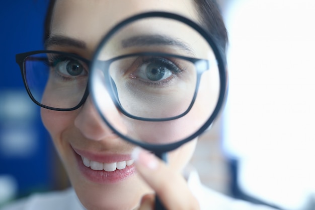 Femme à lunettes regarde à travers la loupe et sourit.