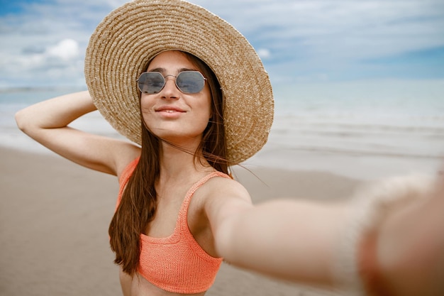Femme à lunettes de soleil debout sur la plage près de la mer pendant les vacances et faisant selfie