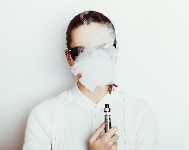 Femme à lunettes de soleil fume une e-cigarette