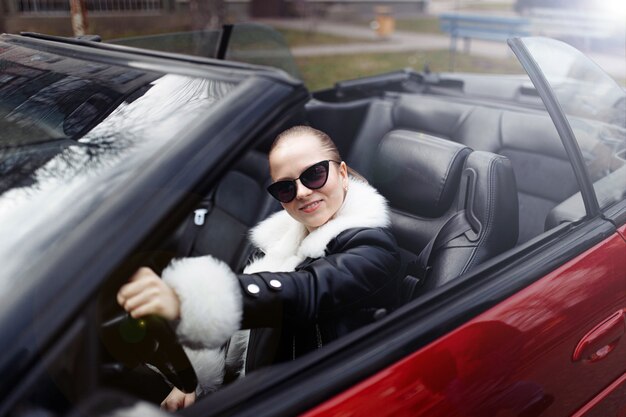 femme à lunettes de soleil et un manteau de fourrure dans un cabriolet