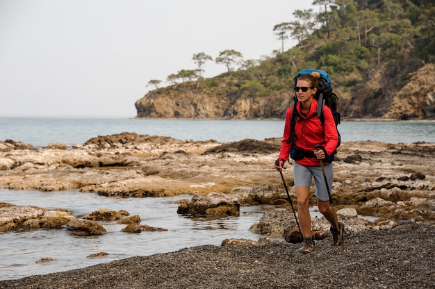 Femme à lunettes de soleil marchant sur les rochers sur la mer avec sac à dos de randonnée