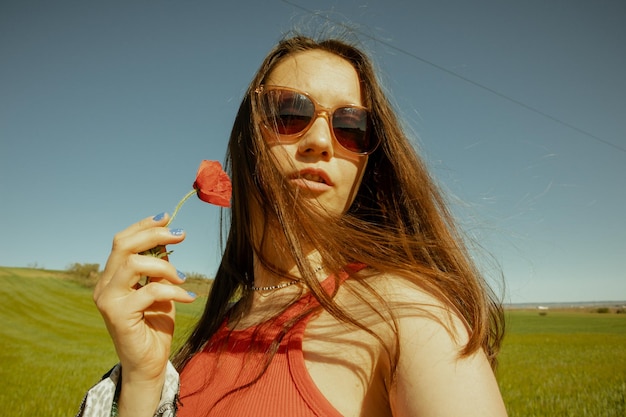 Une femme en lunettes de soleil tient une fleur dans sa main.