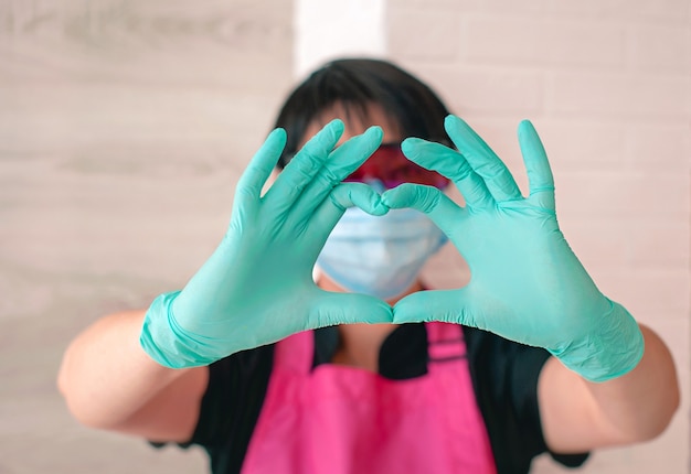 femme à lunettes tablier gants en caoutchouc montrant signe amour par ses doigts Santé