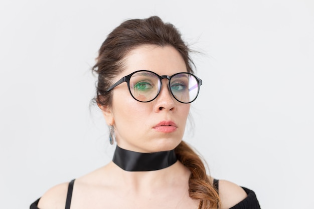 Femme à lunettes et tour de cou sur mur blanc