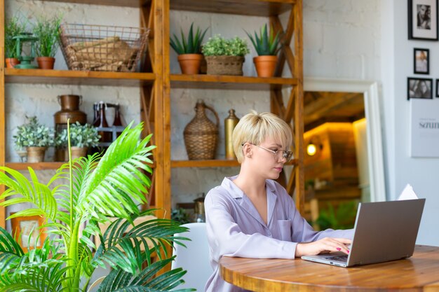 Une femme à lunettes travaille avec des documents devant un écran d'ordinateur portable à l'intérieur de la maison