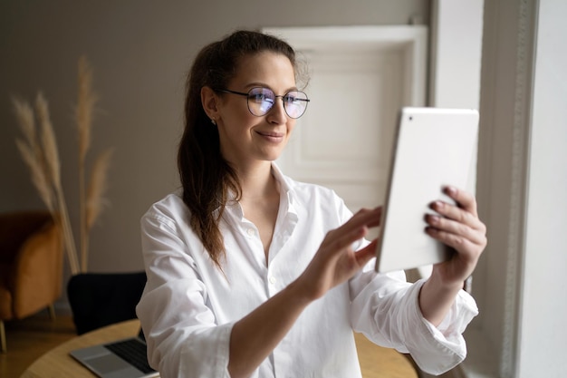 Une femme avec des lunettes utilise une tablette pour appeler des amis vidéo