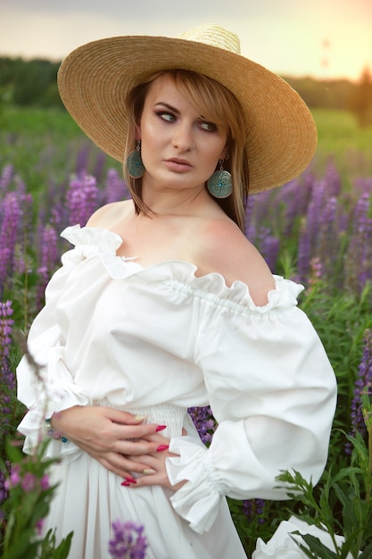 Une femme magnifique dans une longue robe d'été légère et un chapeau sur un champ de fleurs