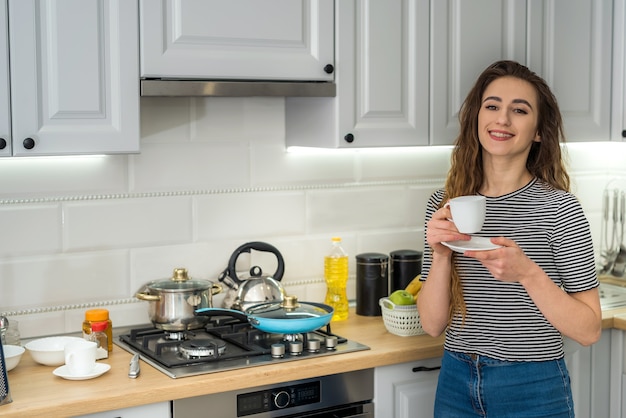 Une femme magnifique se détend le matin dans la cuisine et boit du café. Loisirs à la maison confortable.