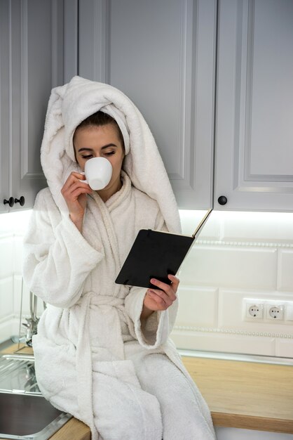 Une femme magnifique se détend le matin dans la cuisine et boit du café. Loisirs à la maison confortable.