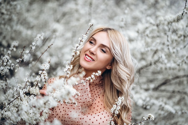 Femme avec un magnifique sourire, des cheveux blonds bouclés en robe rouge s'amusant dans un jardin fleuri