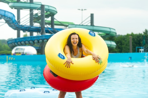 Une femme en maillot de bain avec des cercles gonflables en caoutchouc joue et s'amuse près de la piscine du parc aquatique d'été.