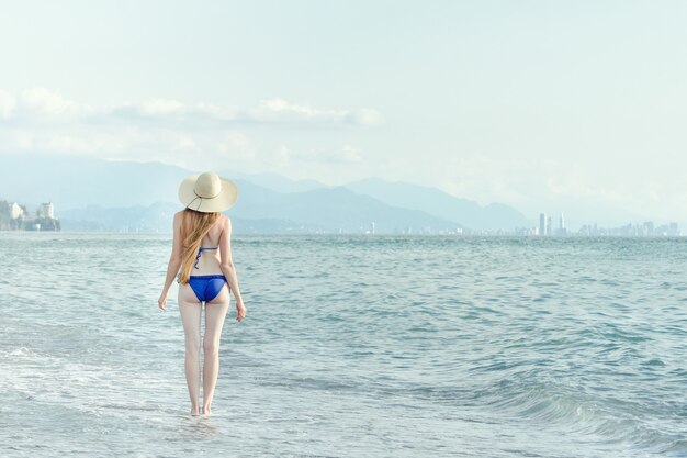 femme en maillot de bain et chapeau se promène au bord de la mer. Vue de l'arrière