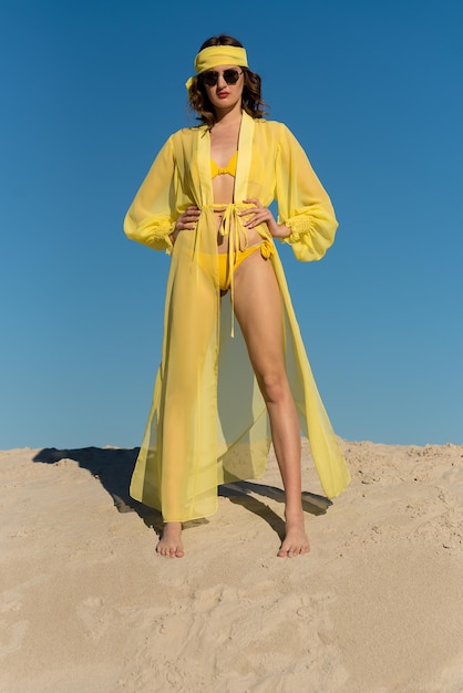 Une femme en maillot de bain jaune se dresse sur une dune de sable.