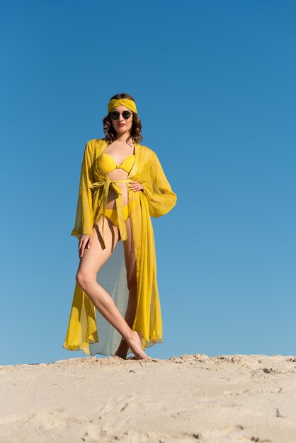 Une femme en maillot de bain jaune se tient sur une plage dans le désert.