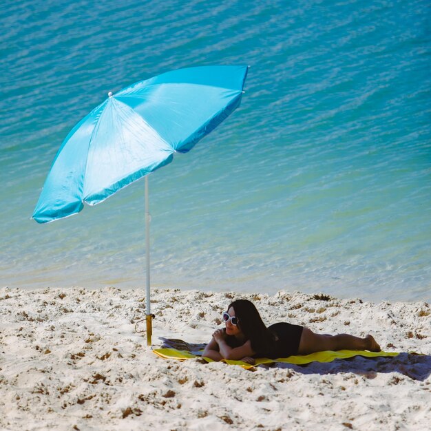 Photo une femme en maillot de bain marchant sur une plage de sable bleu, un parapluie et une couverture jaune.