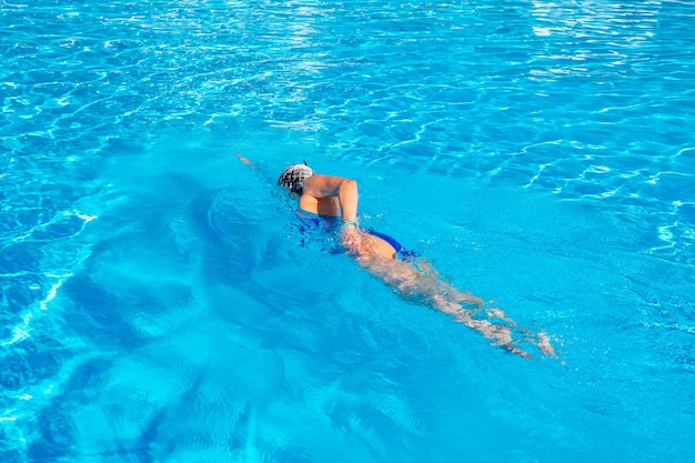 Femme avec maillot de bain nageant sur une piscine d'eau bleue.