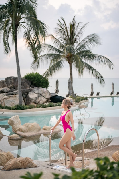 Femme en maillot de bain une pièce rose debout près de la piscine