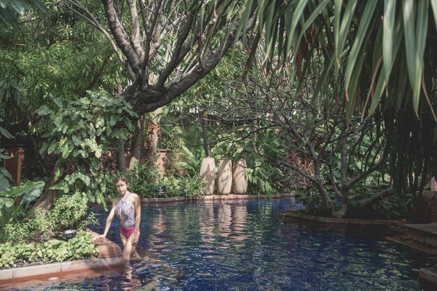 Femme en maillot de bain une pièce rose se détendre dans une piscine tropicale, vacances d'été