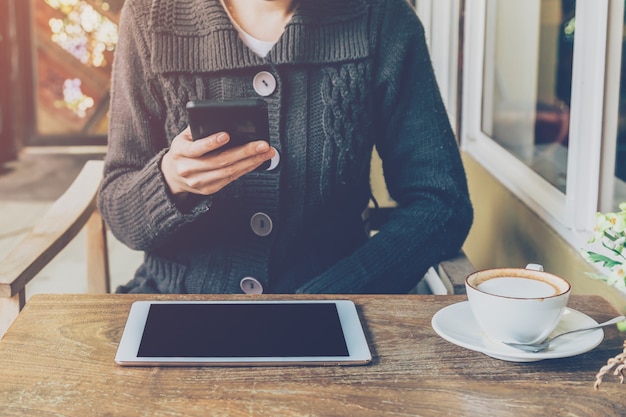 femme de la main à l&#39;aide de smartphone dans un café et une lumière douce avec filtre vintage.