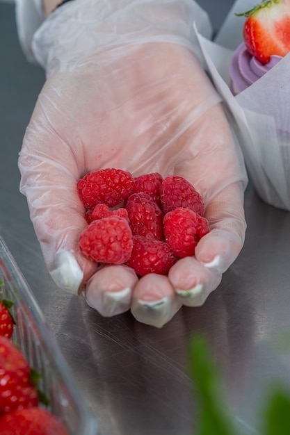 femme main chef dans un gant tient une poignée de framboises pour décorer le gâteau.