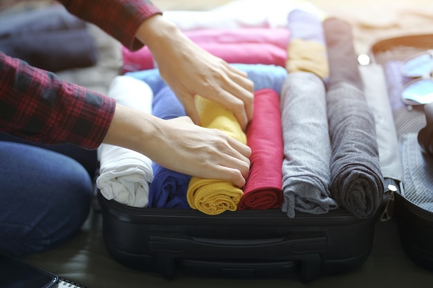 Femme main emballer des vêtements dans un sac de valise sur le lit