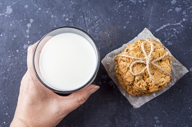 Femme main tenant des biscuits à l'avoine faits maison avec des raisins secs et du chocolat et un verre de lait