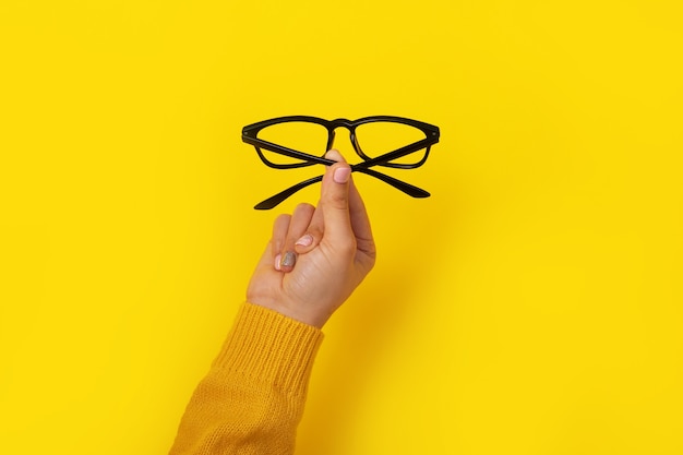 Femme main tenant des lunettes sur jaune