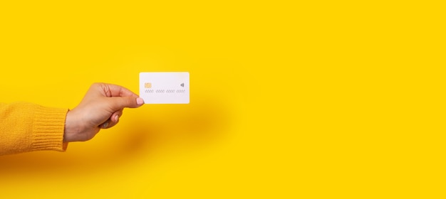 Femme main tenant une maquette de carte de crédit blanche vierge, carte avec puce électronique sur fond jaune