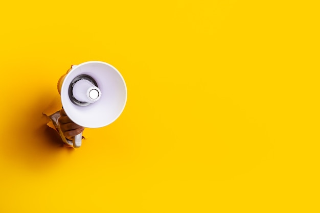 Femme main tenant un mégaphone à partir d'un trou dans le mur sur un fond jaune