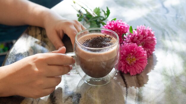 Femme main tenant une tasse de cacao ou de chocolat chaud à côté de fleurs sur table en marbre