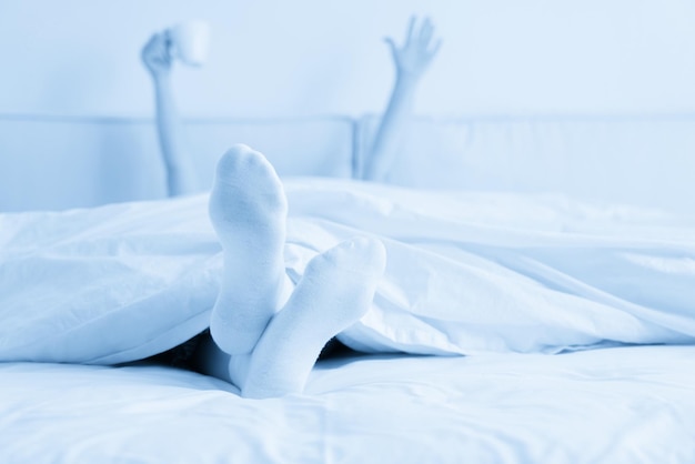 Femme main tenant une tasse de café sous une couverture au lit