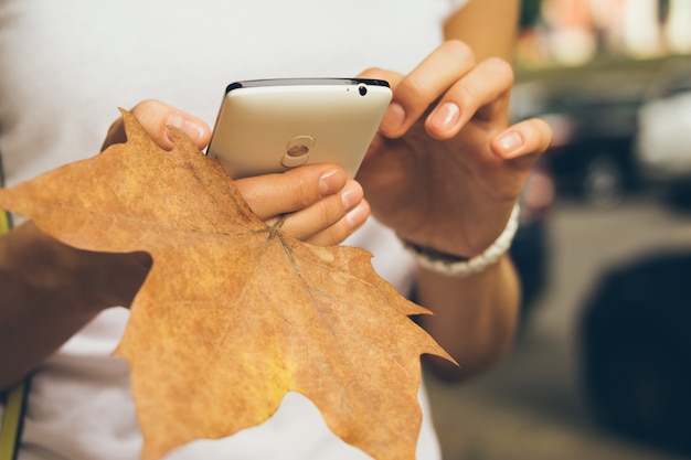 Femme main tenant un téléphone portable et gros plan des feuilles tombées