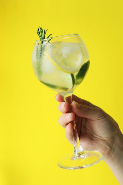 Femme main tenant un verre de cocktail avec des agrumes et du romarin sur une surface jaune