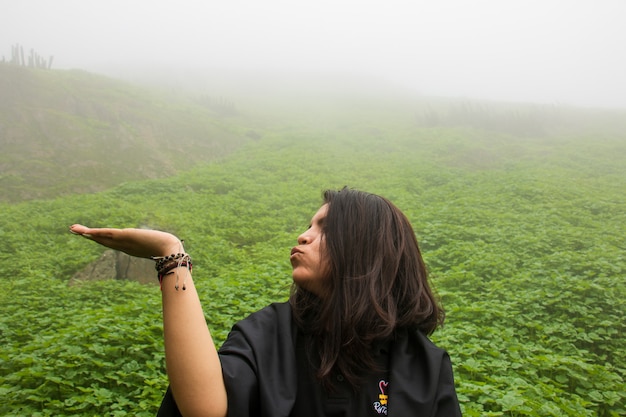 Femme avec la main tendue au milieu d'un paysage vert et nuageux